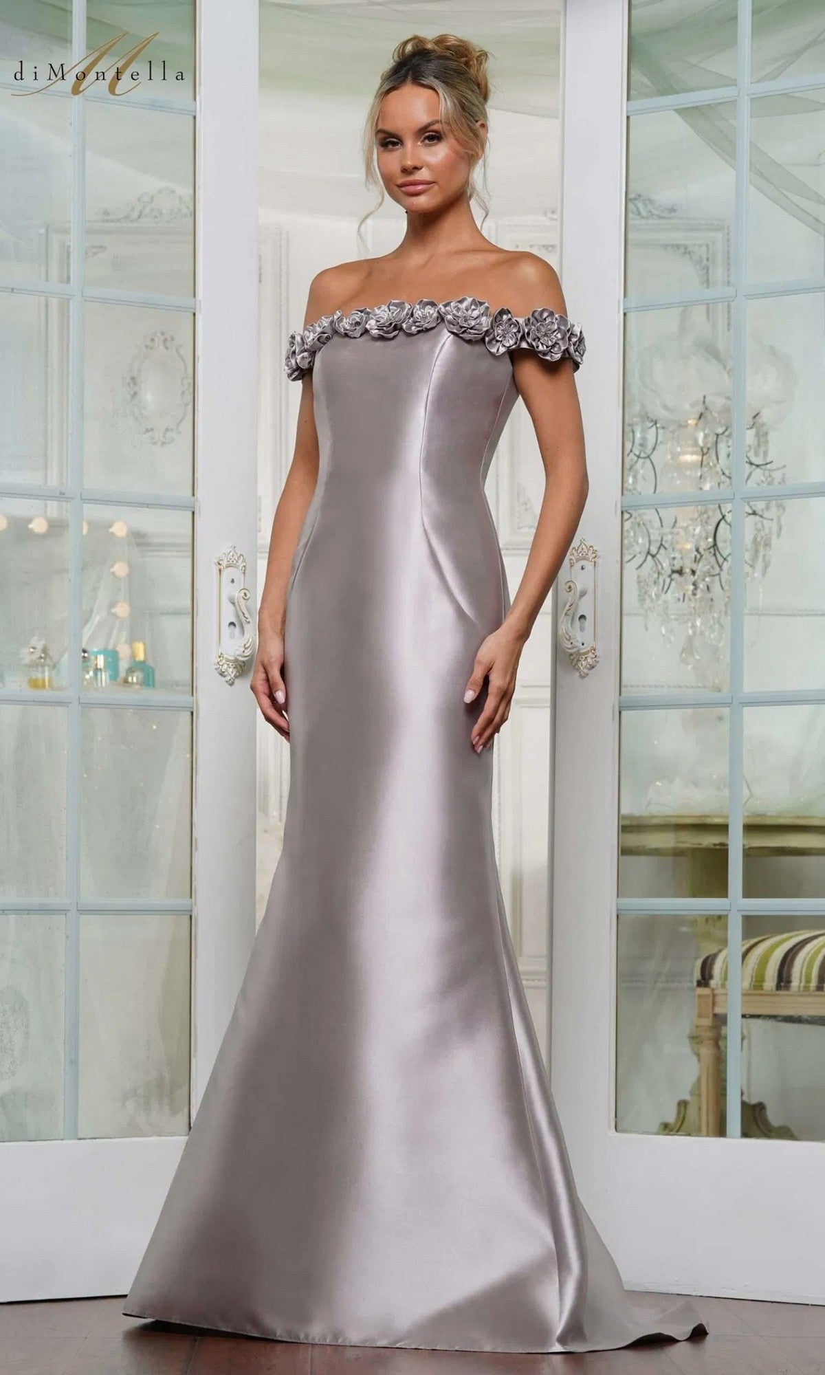 A woman in a taupe Rina Di Montella RD3205 long formal dress with floral detailing and a graceful mermaid silhouette stands before glass doors in an elegant room.